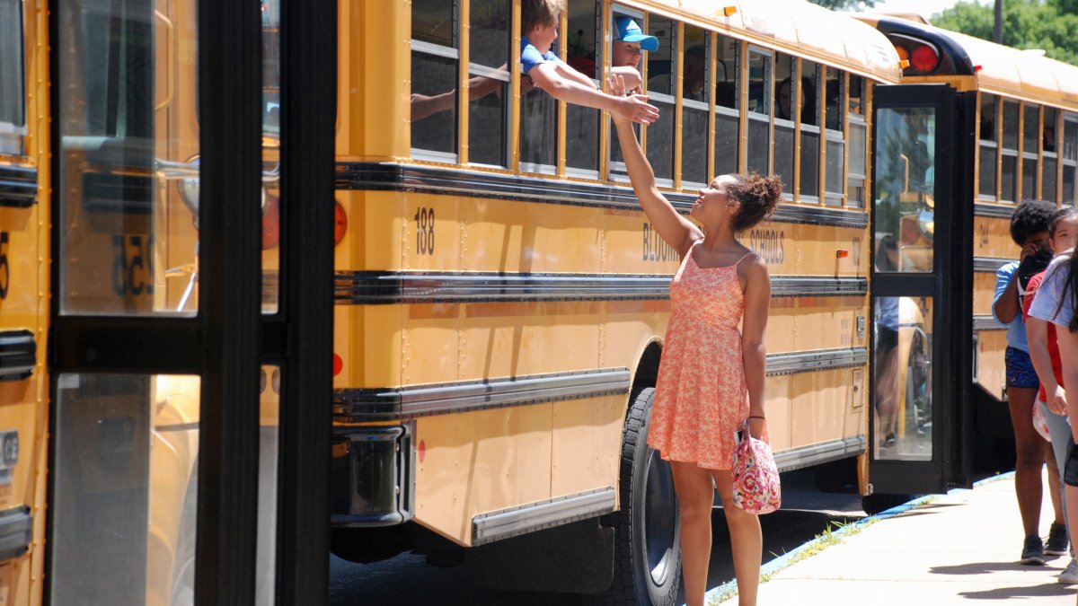 Girl stands next to bus and high fives with someone inside the bus