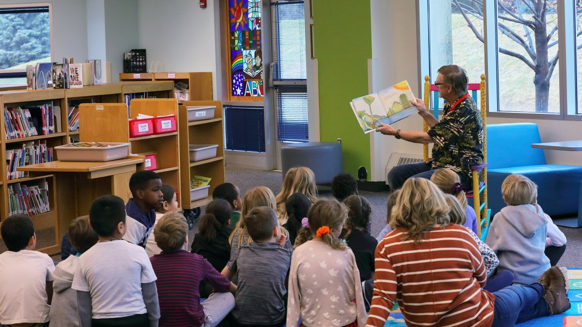 A staff member reads to a group of students in the media center
