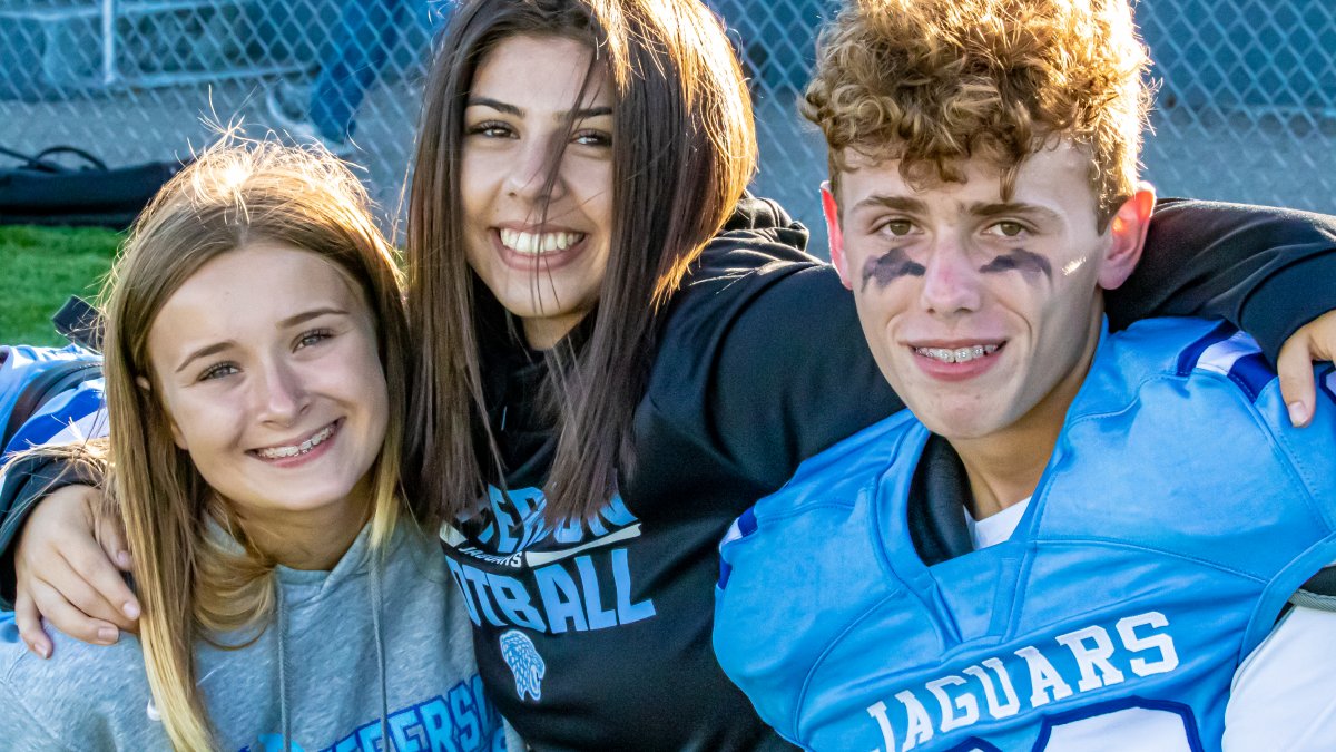 Students wearing Jefferson gear smile during a football game