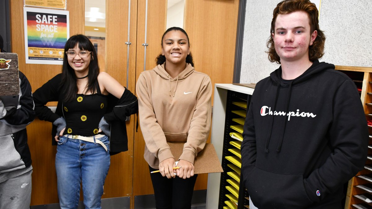 three students standing by a door and smiling