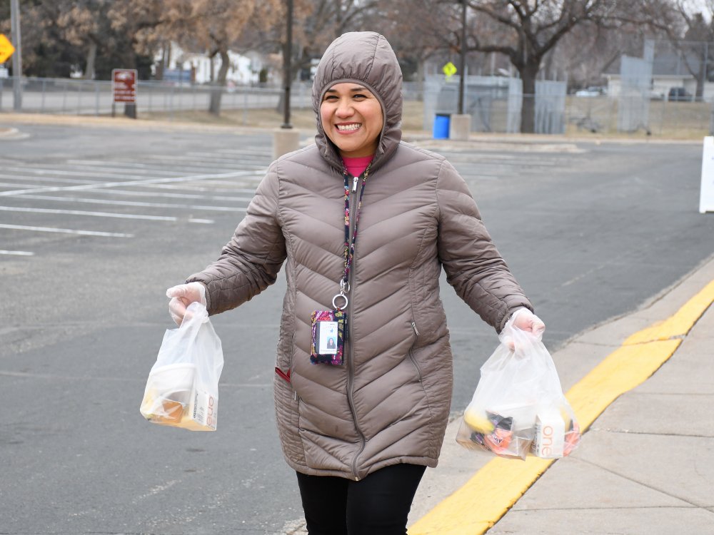 Staff member smiling and holding two bagged meals in each hand