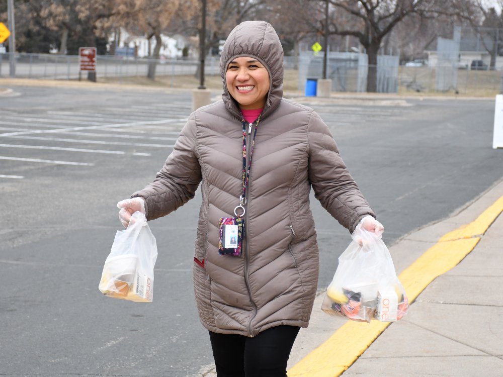 Staff member smiles with bag lunches in each hand