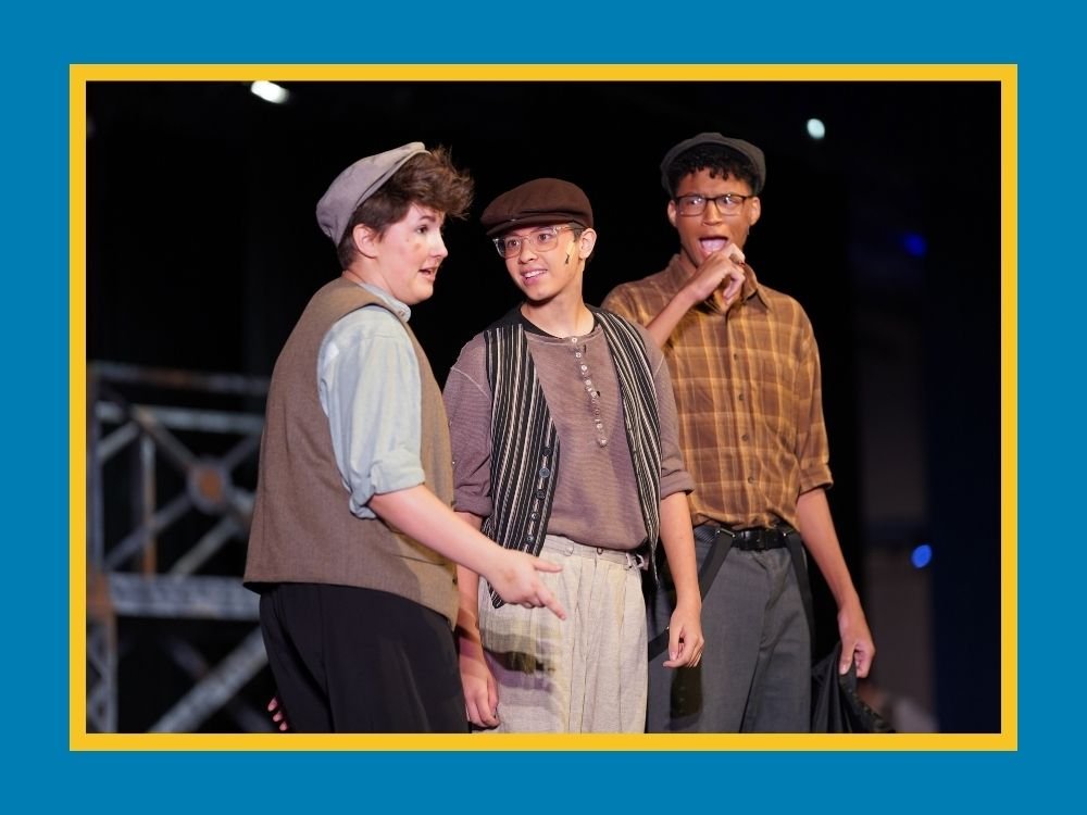 three students performing the musical Newsies on stage