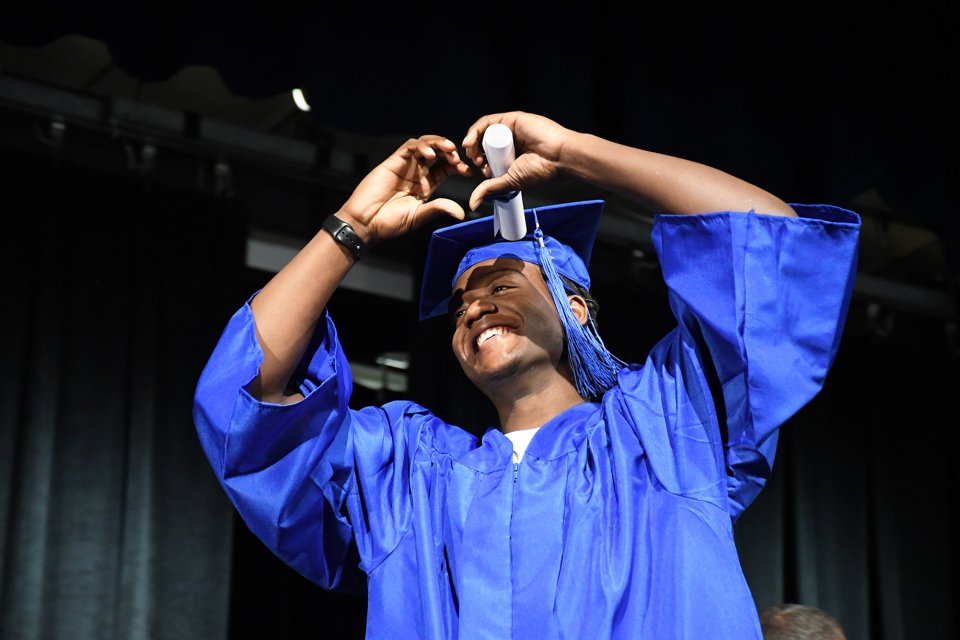 student in cap and gown making a heart with his hands