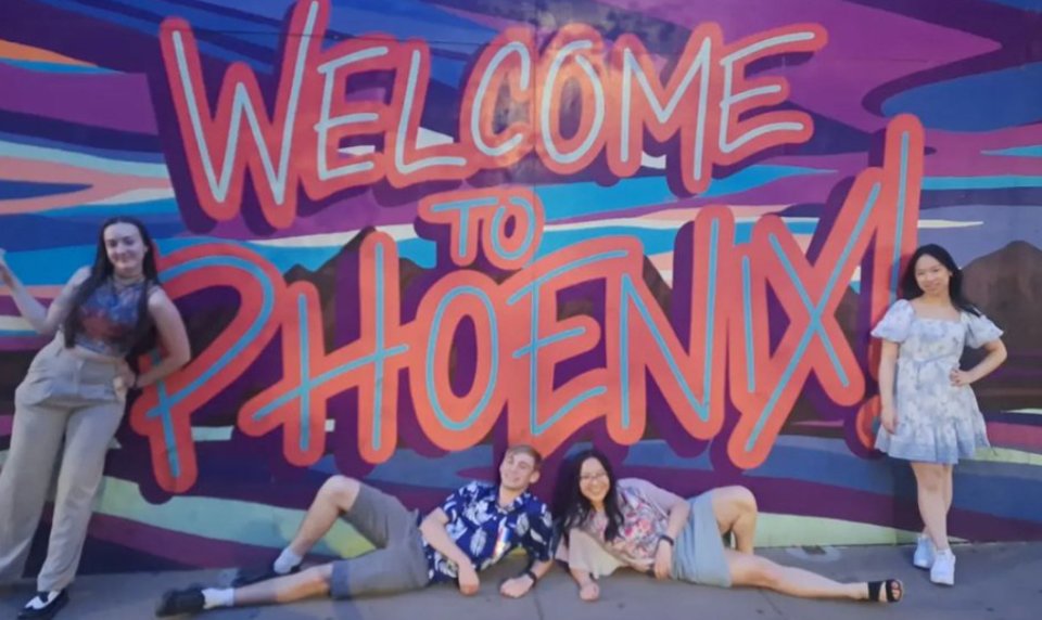 four students in front of a sign that says "Welcome to Phoenix"