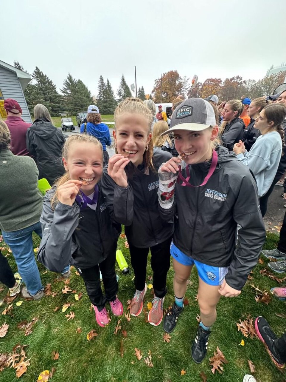 Three girls cross country athletes biting medals