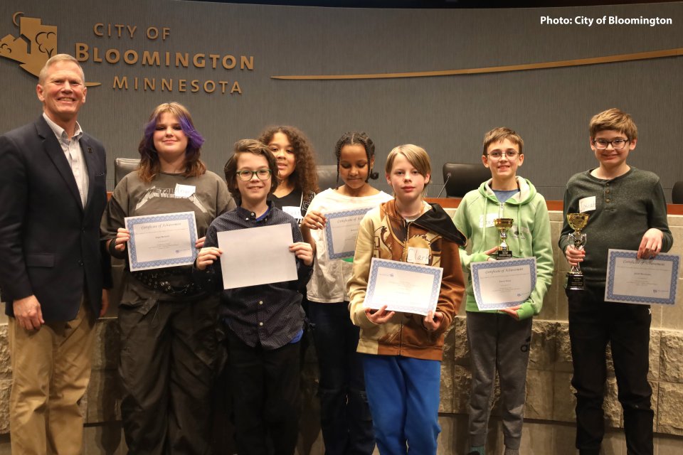 Seven middle school students holding certificates with Bloomington Mayor Tim Busse
